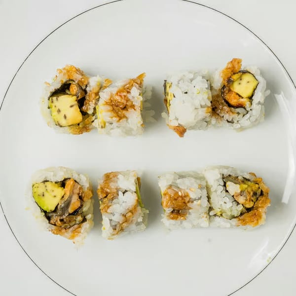 Eight pieces of Kei Sushi rolls with avocado and a brown sauce on a white plate.