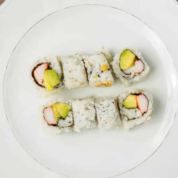 Two rows of Kei Sushi California rolls with crab and avocado on a white plate.