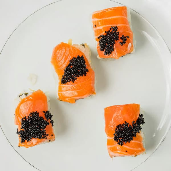 Four pieces of Kei Sushi salmon nigiri, topped with black caviar, arranged on a white plate.