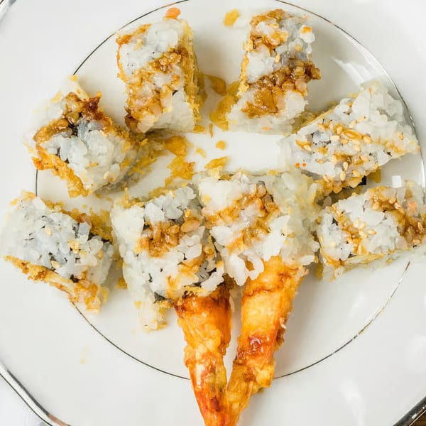 A plate of Kei Sushi Restaurant's crispy shrimp tempura rolls, topped with sesame seeds and sauce.